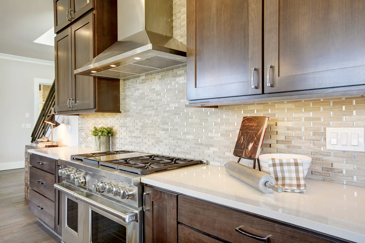 Gas range under a stainless hood with dark wood cabinets and a glass tile backsplash