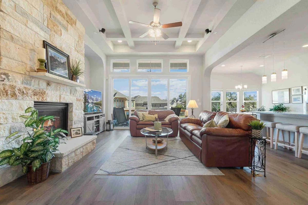 Living room with a stacked stone fireplace, coffered ceiling and a wall of windows