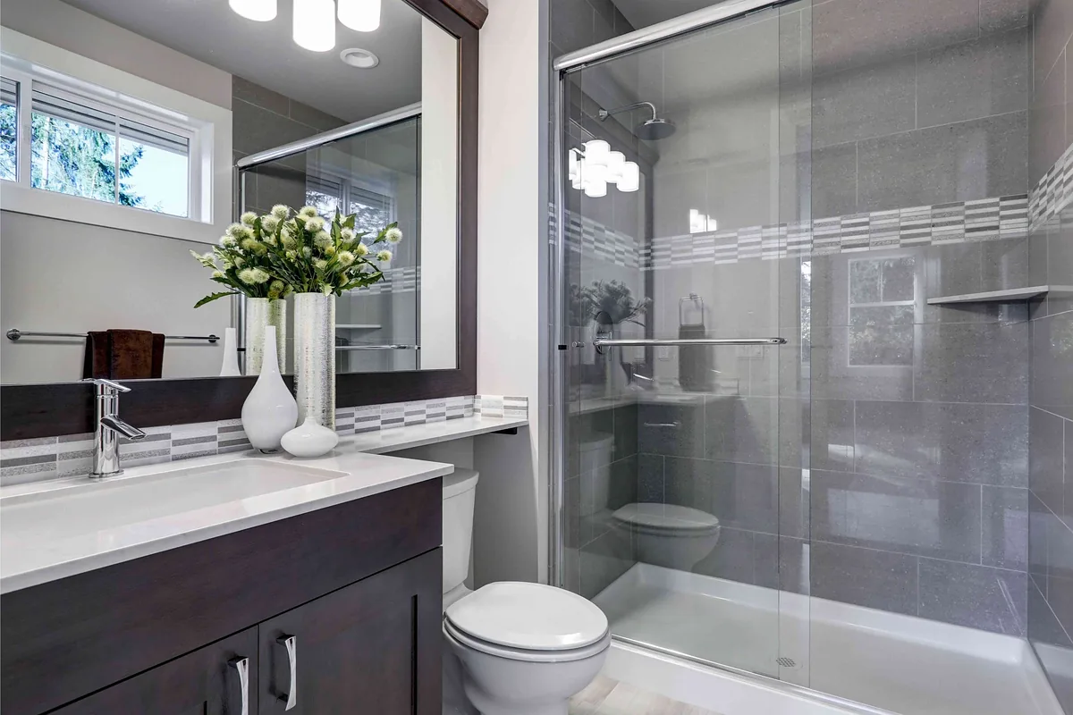 Bathroom with a dark vanity, walk-in glass shower and gray tile
