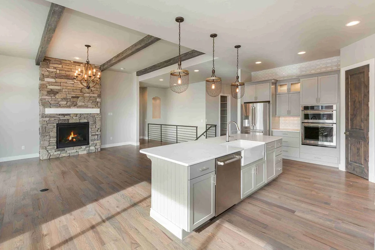 Open kitchen and living area with a stone fireplace, white island and pendant lights
